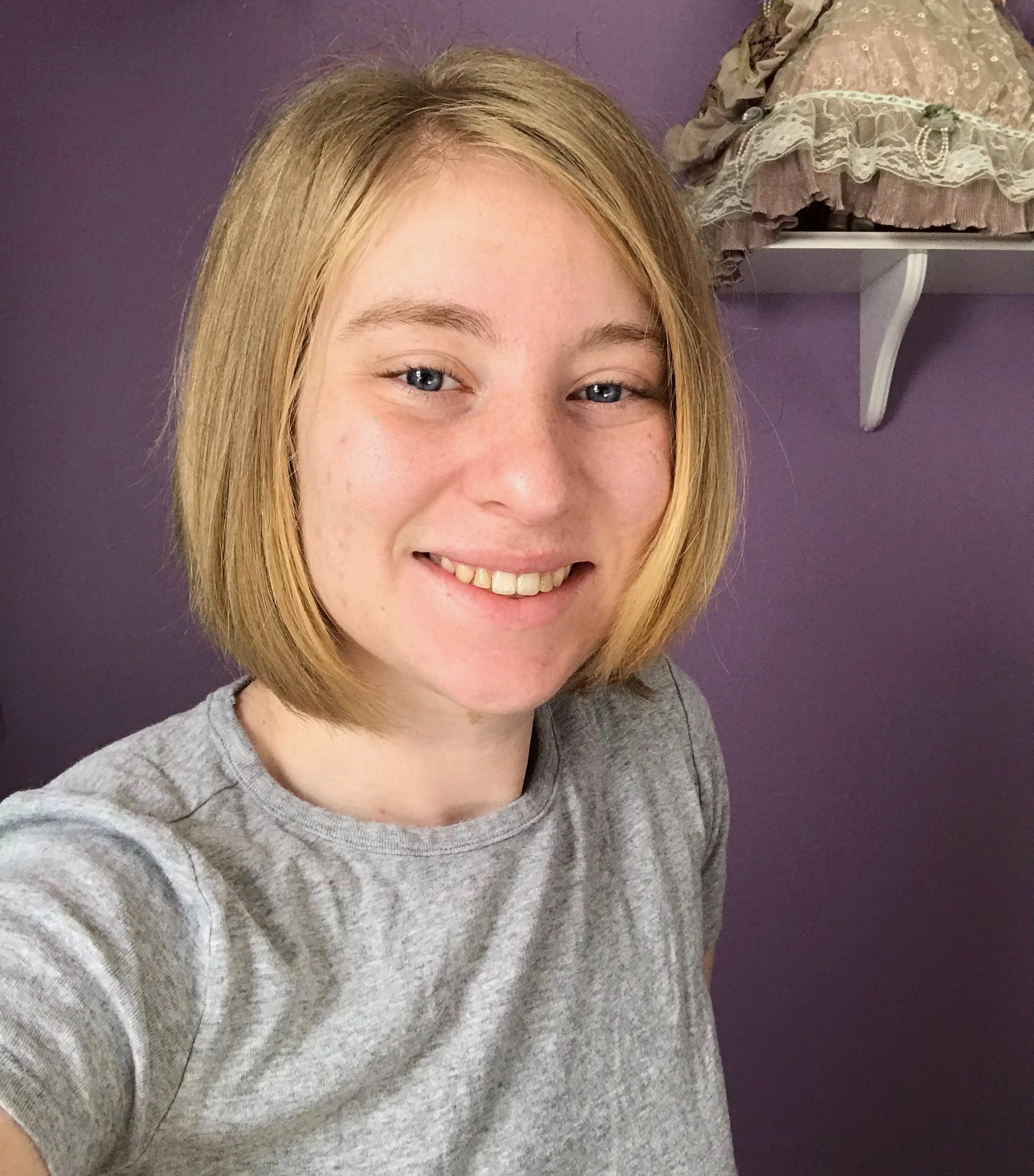 Erica, wearing a gray shirt, smiling with a purple wall behind her. 