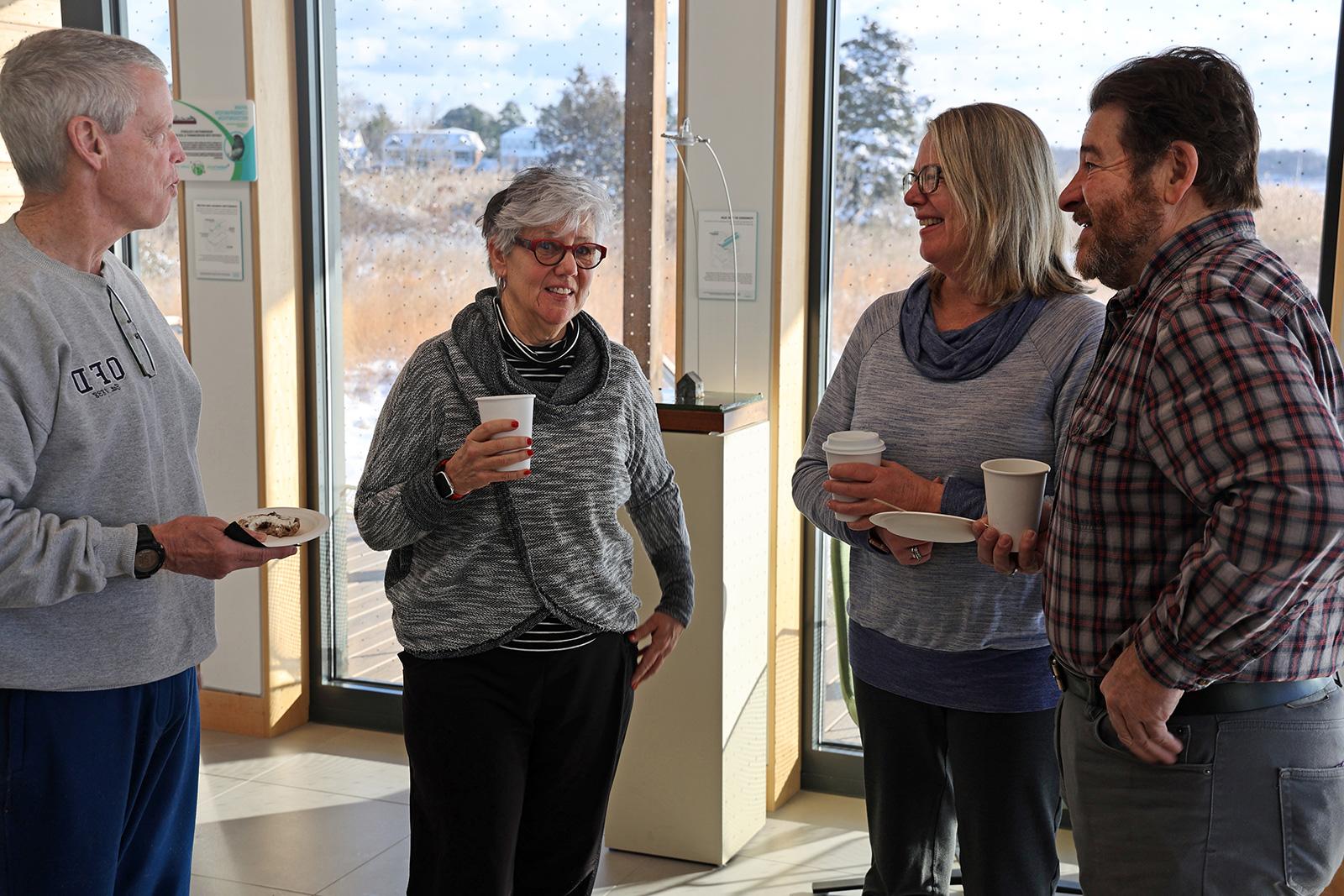 Four people standing, chatting, and drinking coffee