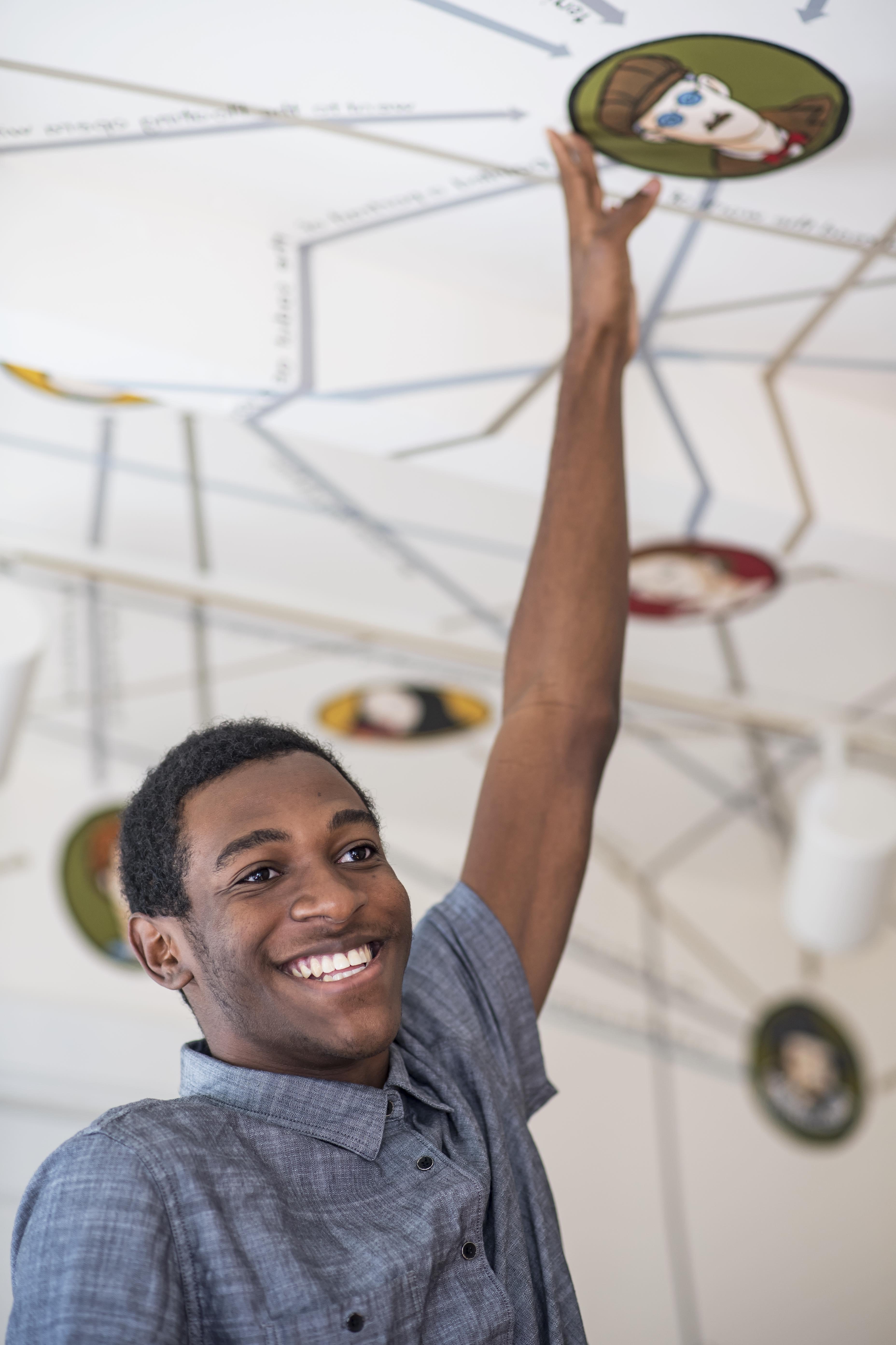 Dante, wearing a blue shirt, smiling as he reaches towards the ceiling of the Rose O'Neill Literary House.